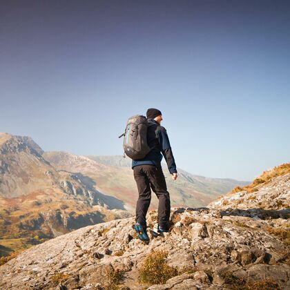 A lone make hiker with backpack walks away from the camera and toward the Welsh mountains.